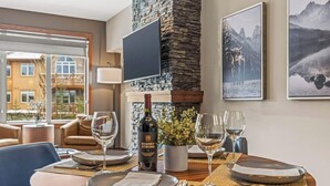 A dining area with a table set for two, a bottle of wine, and a potted plant. - Hope Peak Hydeaway at Stoneridge (Canmore)