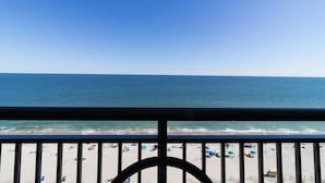 Blick auf einen Strand vom Balkon mit Geländer, klarer Himmel und Meer.