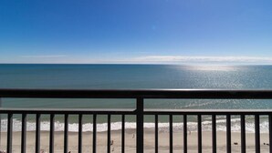 Vista a la playa desde un balcón con barandilla, mar y cielo despejado.