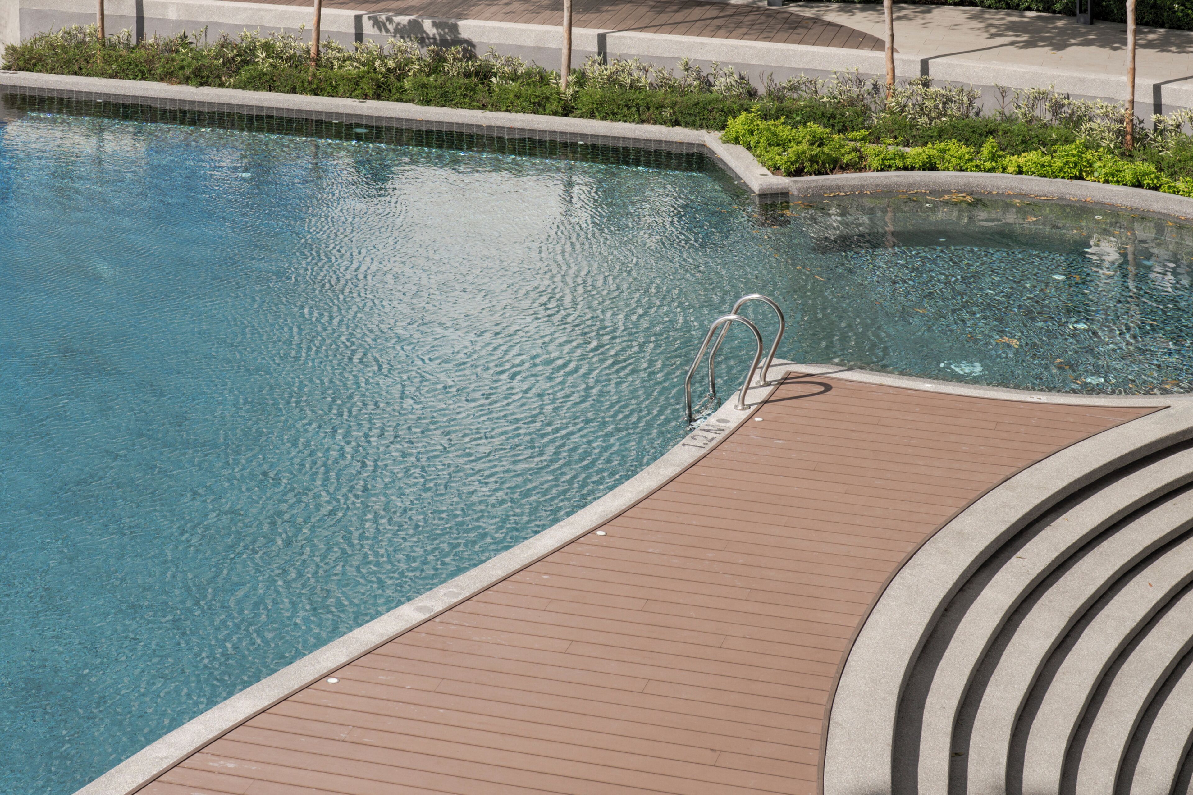 A swimming pool with a wooden deck and metal handrails.