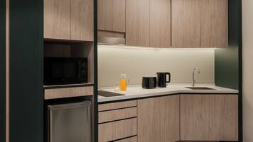 A modern kitchen with wooden cabinets, a stainless steel refrigerator, a microwave, a coffee maker, and a sink.