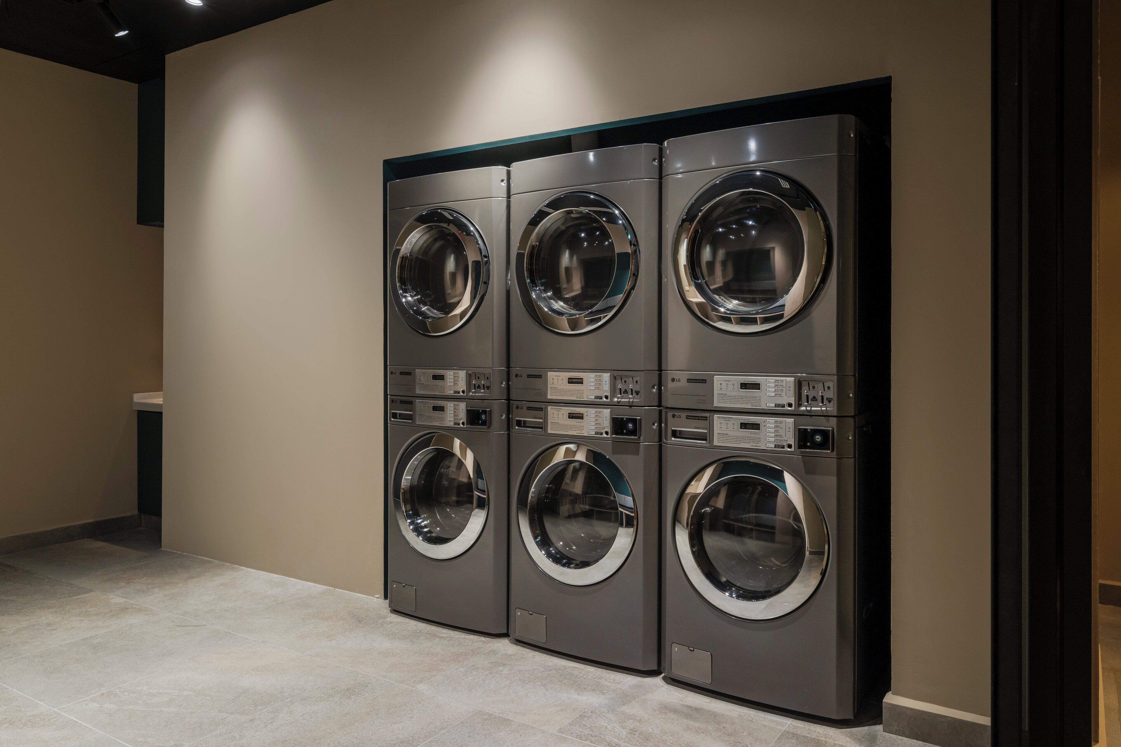 A row of four front-loading washing machines in a commercial setting.