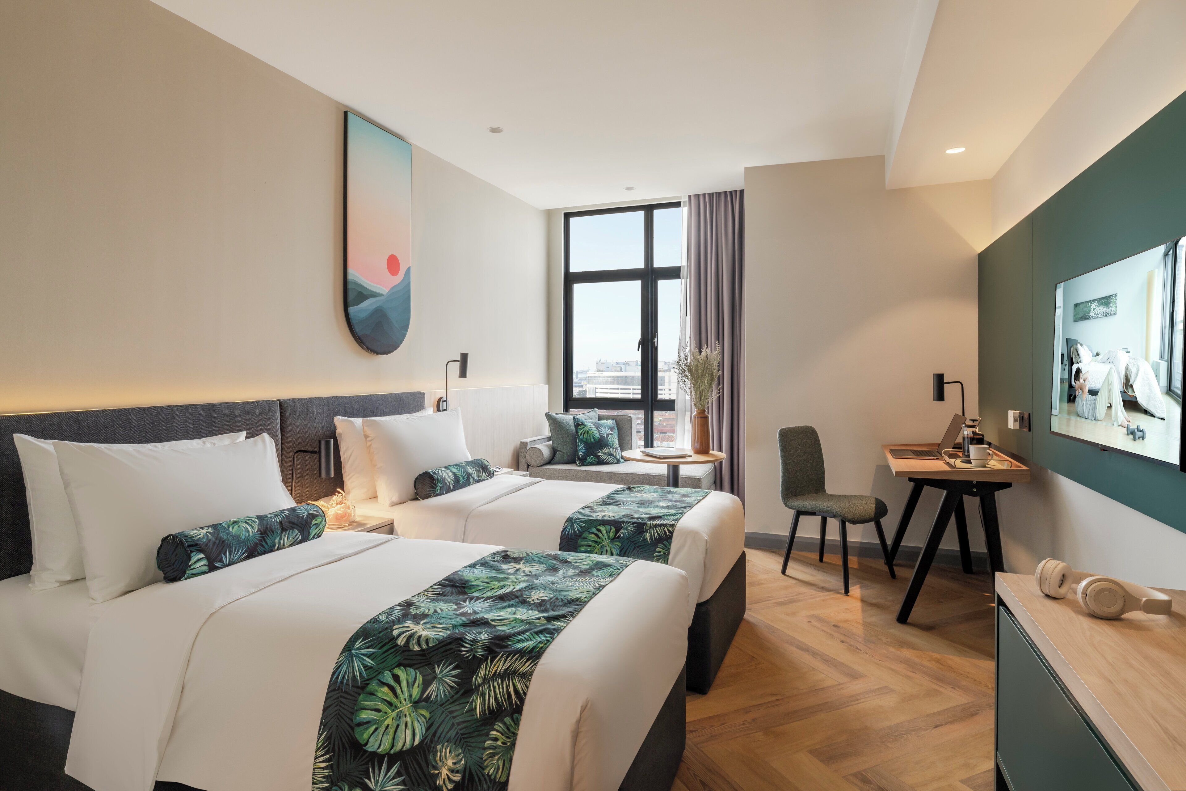 Habitación de hotel con dos camas, un escritorio, una silla y un ventanal grande.