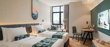 Habitación de hotel con dos camas, un escritorio, una silla y un ventanal grande.