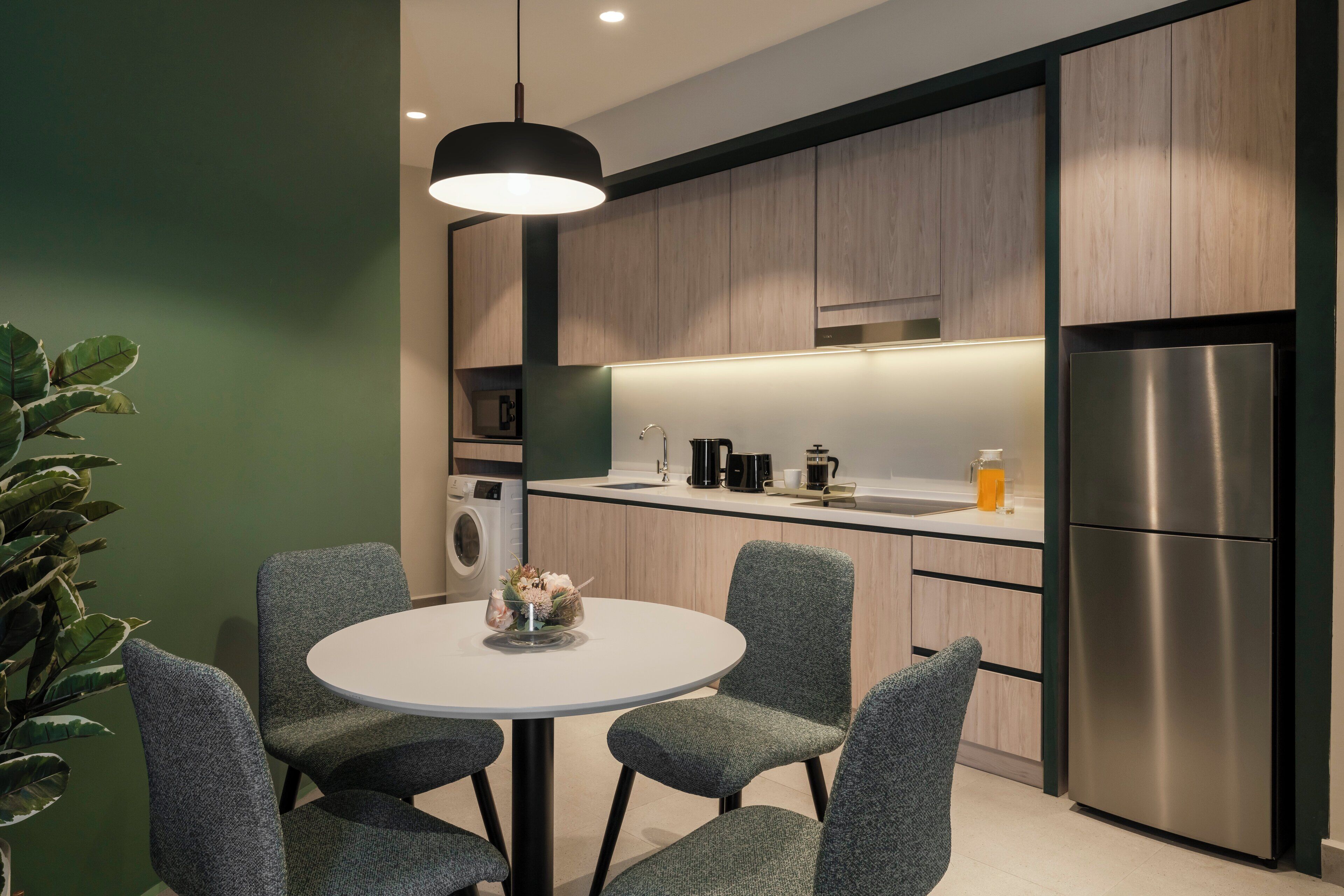 Una cocina moderna con una mesa de comedor redonda, cuatro sillas, una cafetera, un refrigerador y una lámpara colgante.