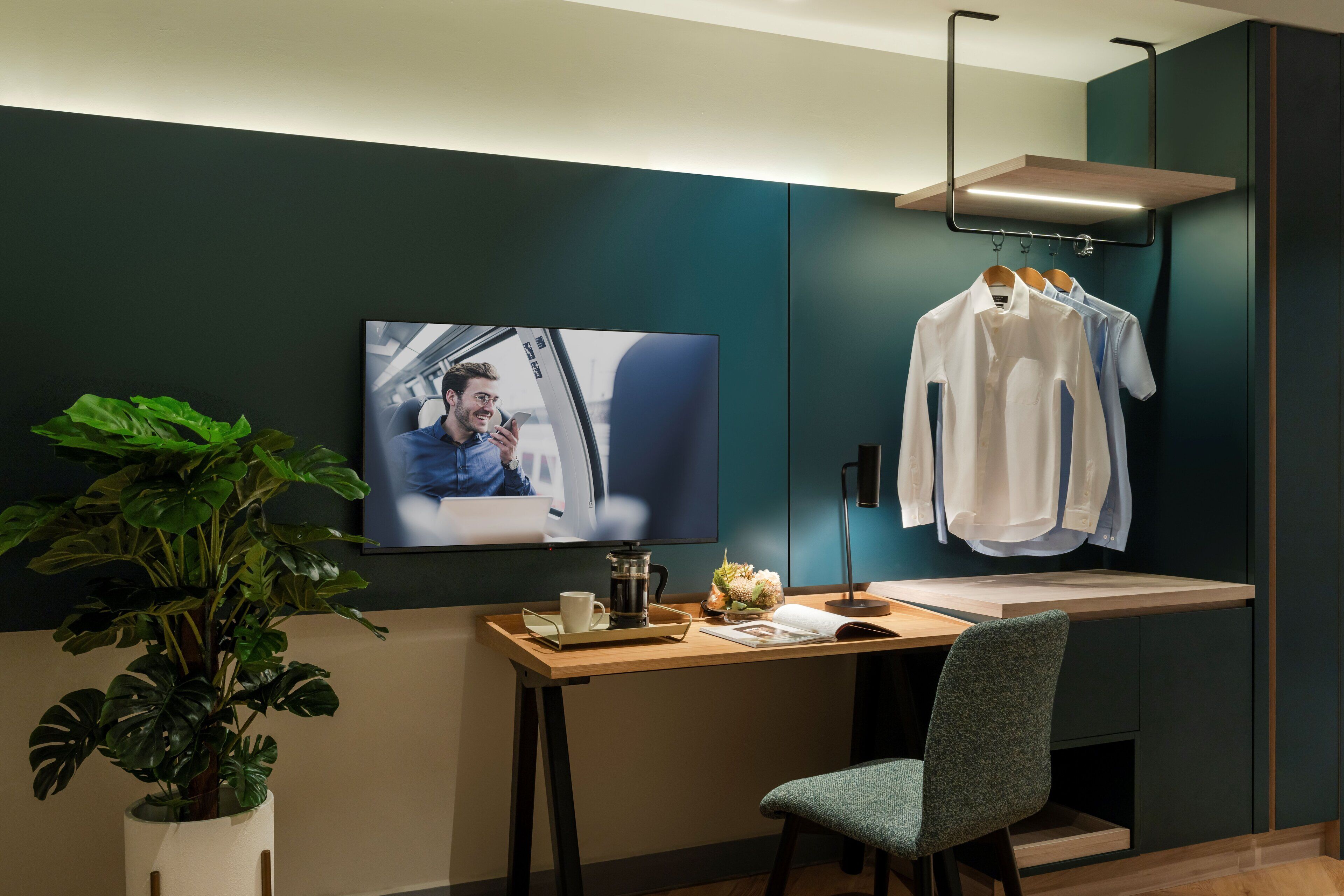 A modern room with a desk, a television, a plant, and a clothing rack.
