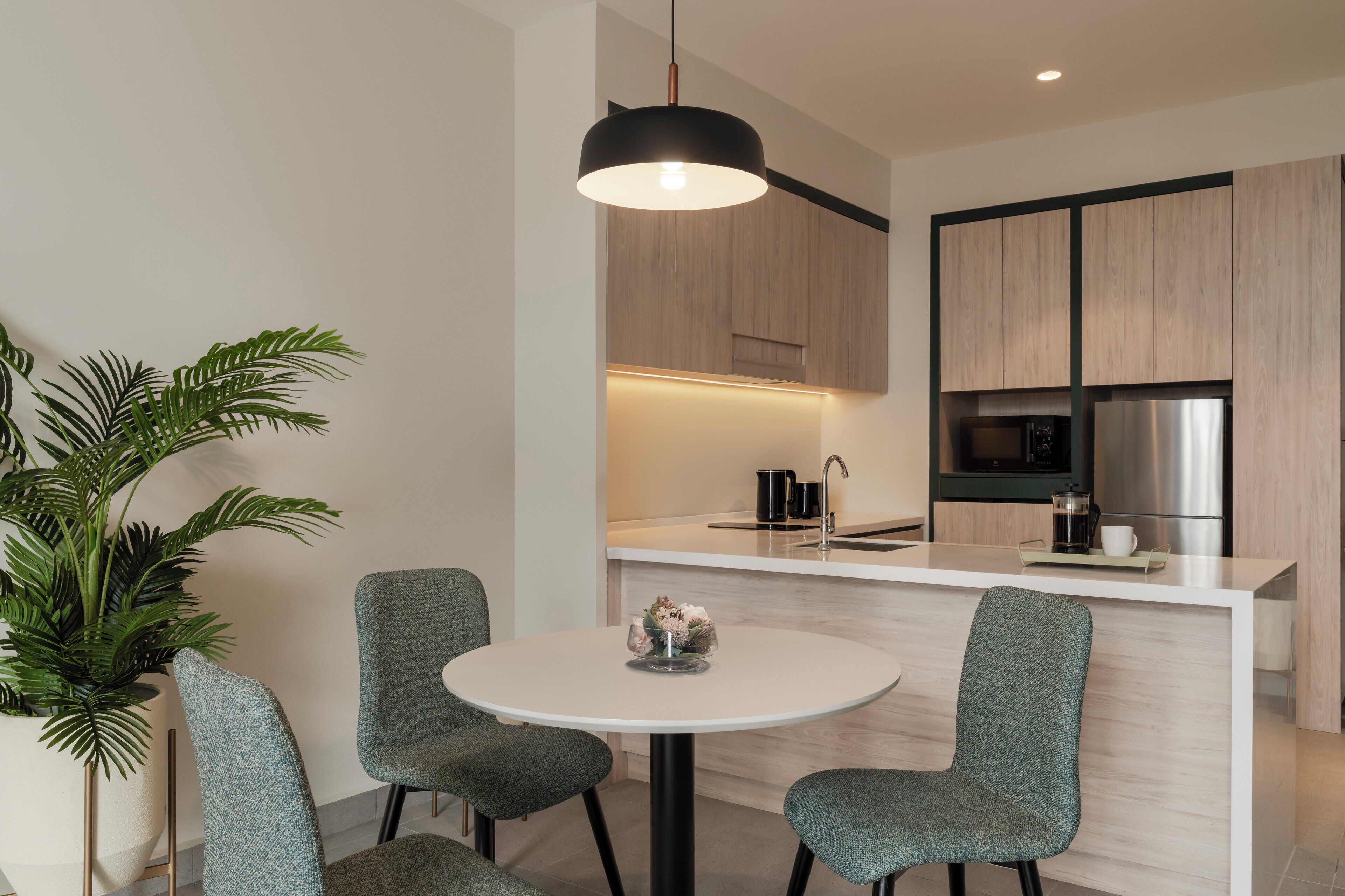 A modern kitchen with a central island, two chairs, a hanging light fixture, and a potted plant.