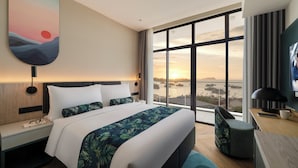 A modern hotel room with a large bed, a desk, and a view of the sunset through large windows. - Citadines Waterfront Kota Kinabalu (Kota Kinabalu)