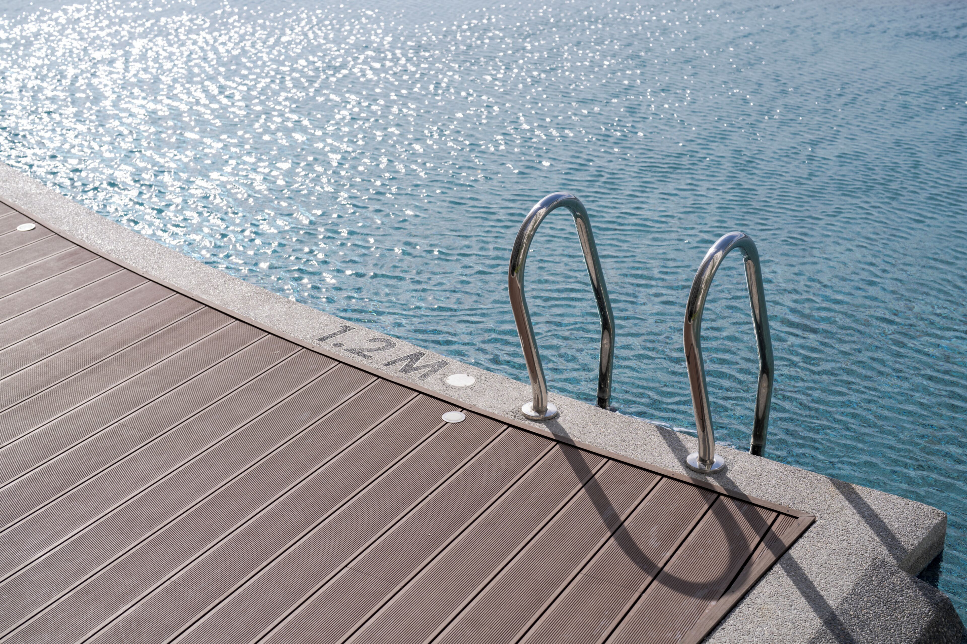 Una terraza de madera con escalones metálicos junto a la piscina que desagua en una piscina azul cristalina.