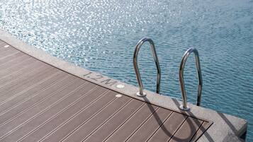 Una terraza de madera con escalones metálicos junto a la piscina que desagua en una piscina azul cristalina.