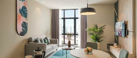 A modern hotel room with a sofa, coffee table, dining table, and a large window with curtains.