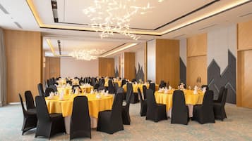 A banquet hall with round tables, black chairs, and yellow tablecloths.