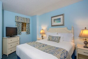 Quarto de hotel com uma cama, televisão em uma cômoda, janela com cortinas e um quadro na parede.