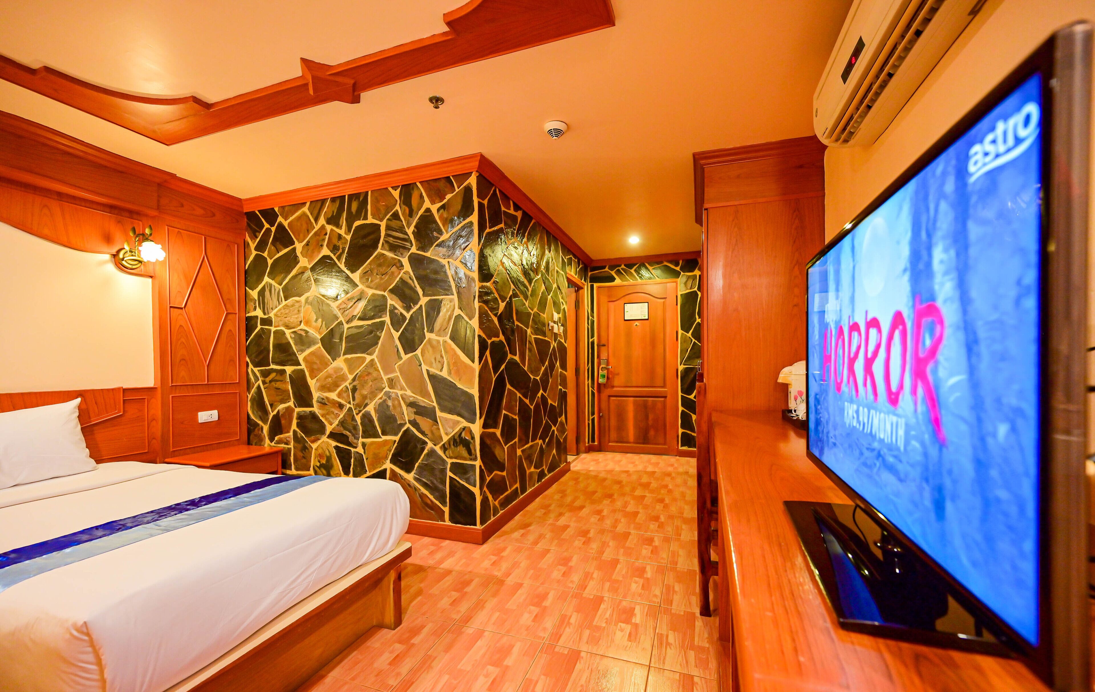 A hotel room with a bed, a television, a stone wall, and a wooden floor.