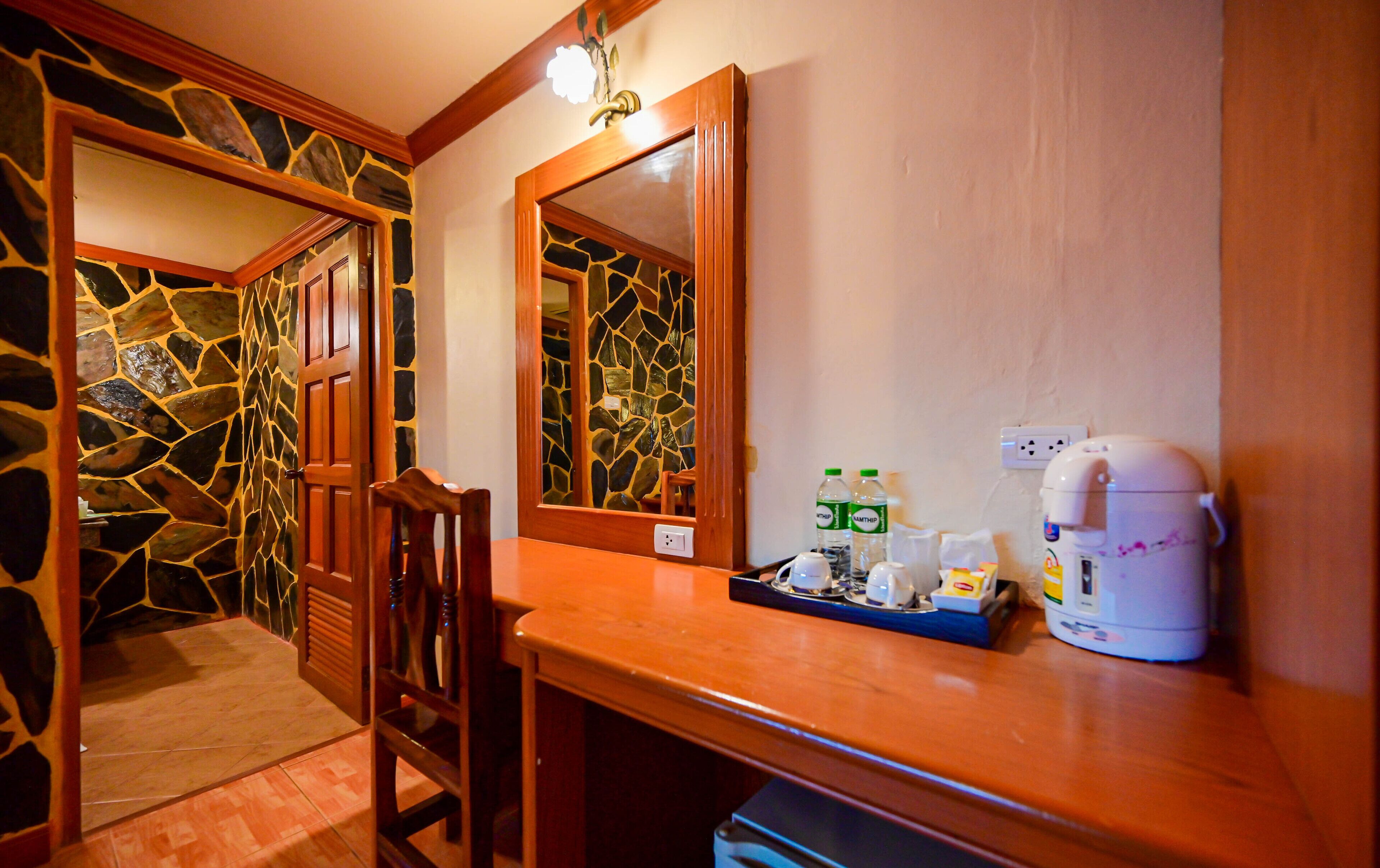 Habitación de hotel con pared de piedra, puerta de madera y mostrador de madera con cafetera, botellas y hervidor.