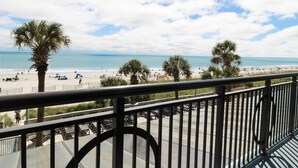 Ein Balkon mit Blick auf einen Strand, Palmen und einen klaren Himmel.