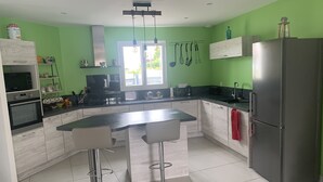 Et moderne køkken med en central ø, barstole, et køleskab og et vindue med naturligt lys.