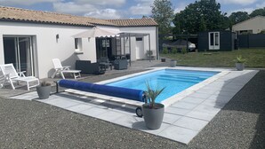 En have med swimmingpool, udendørs møbler og en overdækket terrasse.