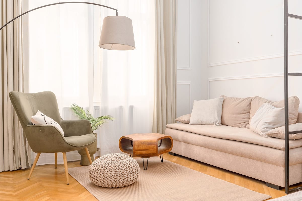 Un salon moderne avec un canapé, un fauteuil, un pouf et une lampe sur pied.