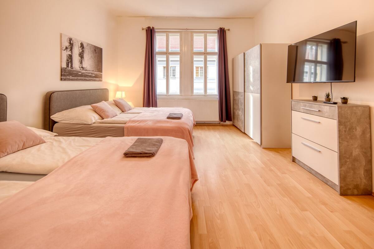 Une chambre d’hôtel avec deux lits, une télévision, une commode et une fenêtre avec des rideaux.
