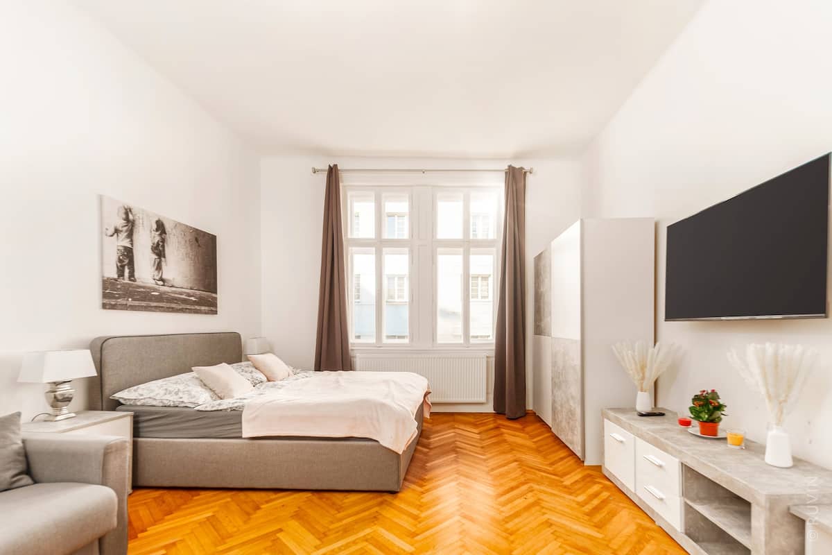 Une chambre à coucher avec un lit, une table de chevet, une lampe et une fenêtre avec des rideaux.