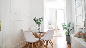 A dining area with a glass table and white chairs, a vase with flowers, and a potted plant. - City Apartment - 5 min to Metro (Vienna)