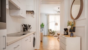 A modern kitchen with white cabinetry, a built-in washing machine, and a dining area with a chair and table. - City Apartment - 5 min to Metro (Vienna)