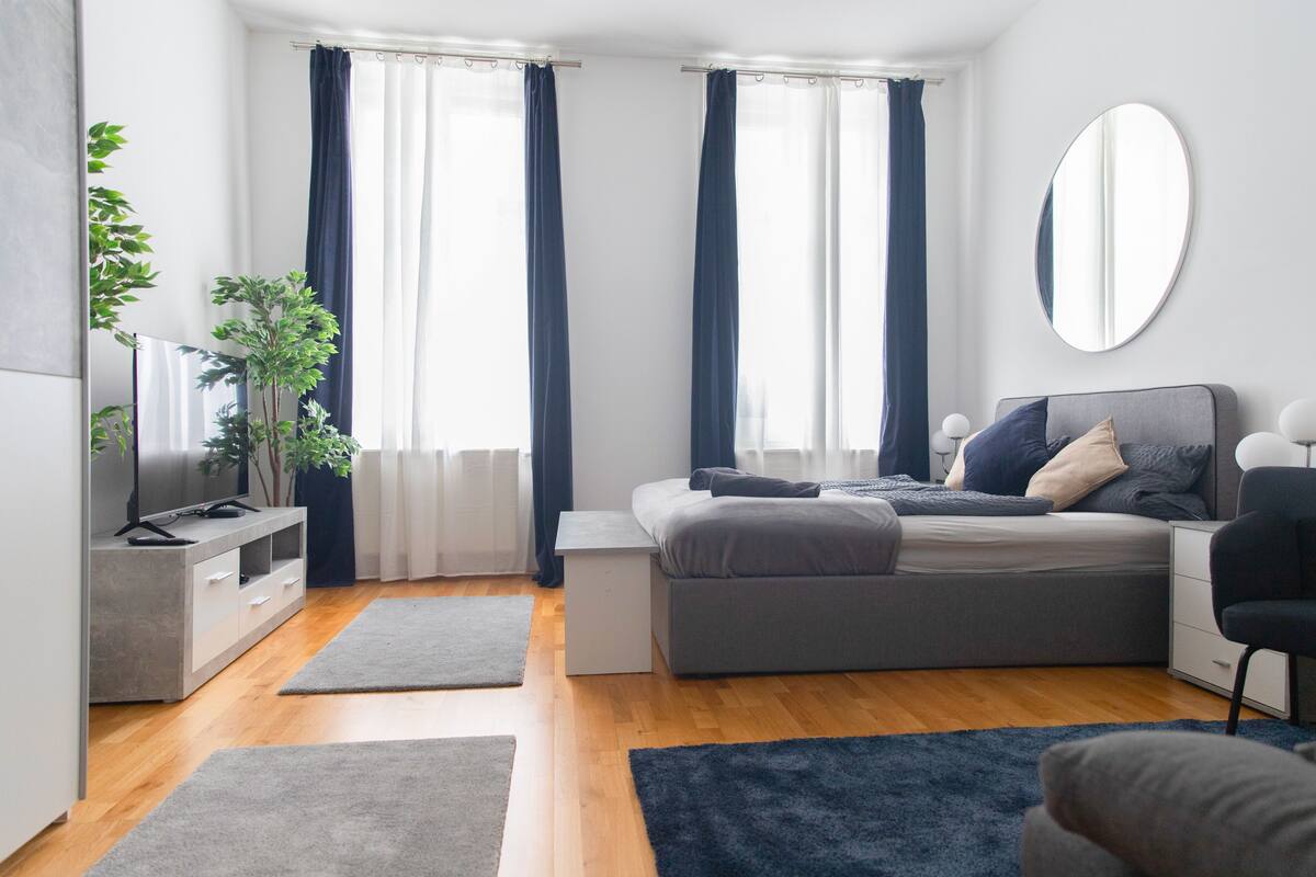 Une chambre à coucher moderne avec un canapé gris, une petite table de chevet, un téléviseur et un grand miroir.