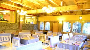 Ein Restaurant mit Holzbalken und Steinwänden, Tische gedeckt mit Besteck und Gläsern, und eine Kristallleuchter.