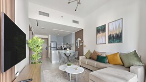 A modern living room with a sofa, coffee table, and TV. There is a kitchen in the background. - WelHome - Contemporary 1BR in Binghatti Canal & Burj Views (Dubai)