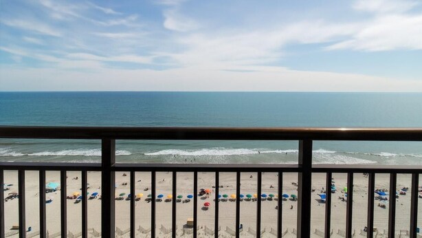 A beach view from a balcony with a railing, sandy beach, and ocean. - 14th Floor Skyline Retreat: 1 Bedroom King Suite (Myrtle Beach)