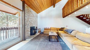 A cozy living room with a stone wall, wooden ceiling beams, a sofa, and a fireplace.