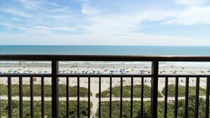 Vista a la playa desde un balcón con barandilla, playa de arena y océano.