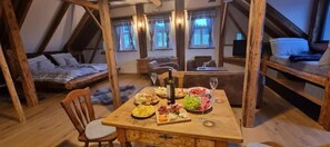 Acogedor cuarto ático con una mesa de madera preparada para una comida, una cama y un televisor al fondo.