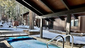 Une piscine extérieure couverte, recouverte d’une bâche bleue au fond, entourée de neige et d’arbres.