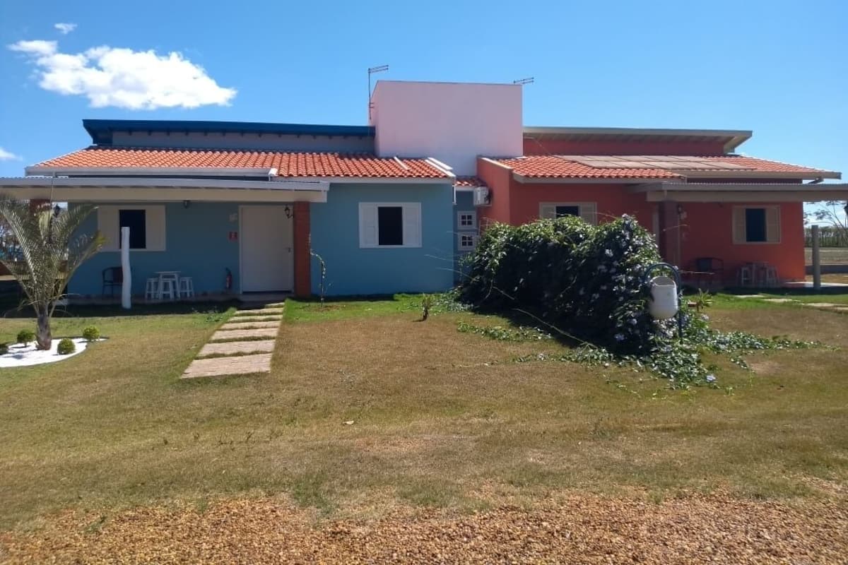 A two-story house with a red-tiled roof, a small garden with a pathway, and a white building adjacent to it.