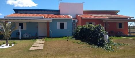 A two-story house with a red-tiled roof, a small garden with a pathway, and a white building adjacent to it.