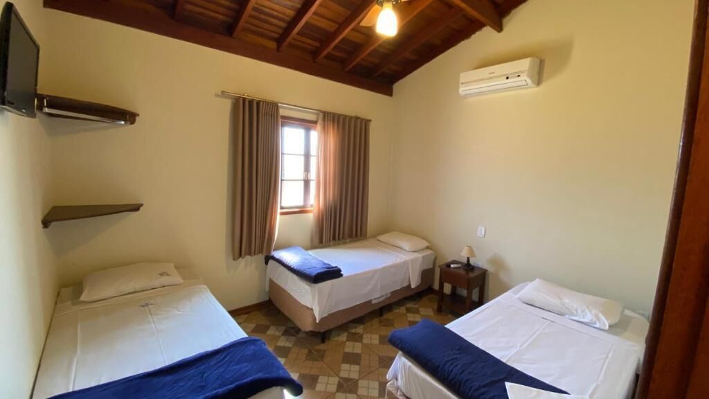 A room with two beds, a window with curtains, a heater, and a small table.