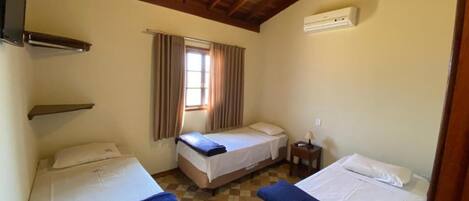 A room with two beds, a window with curtains, a heater, and a small table.
