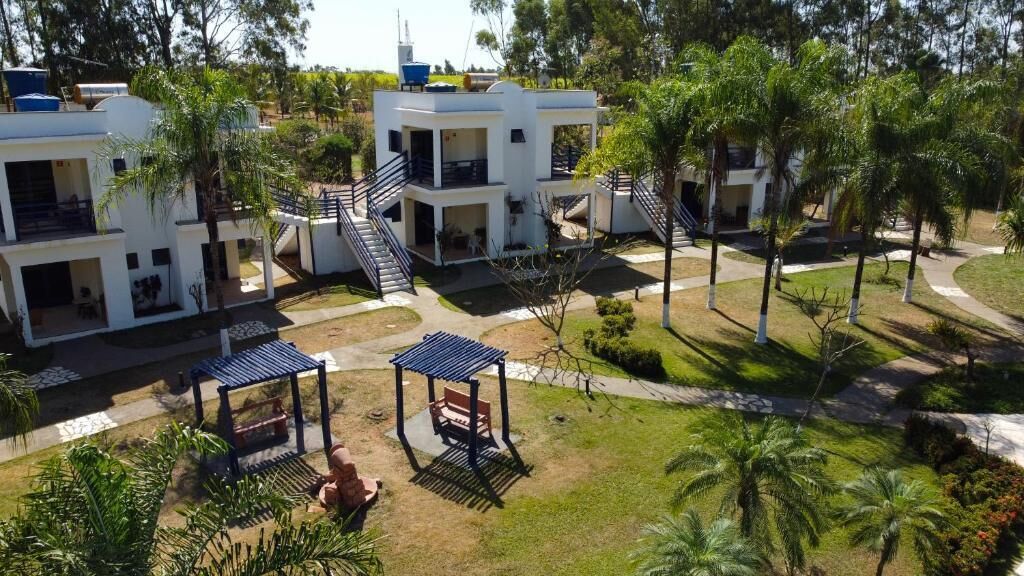 A modern multi-story building with balconies, a covered seating area, and a well-maintained garden with palm trees.