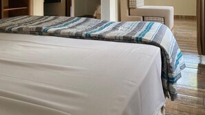 Quarto de hotel com cama, televisão fixada na parede, janela com vista para área verde e banheiro com toalha pendurada.
