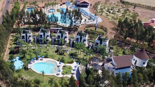 Vista aérea de um resort com vários edifícios, uma piscina central ampla e vegetação ao redor.
