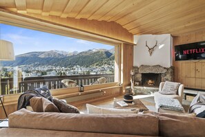 A cozy living room with a large window overlooking a mountainous landscape, a fireplace, and a Netflix sign.