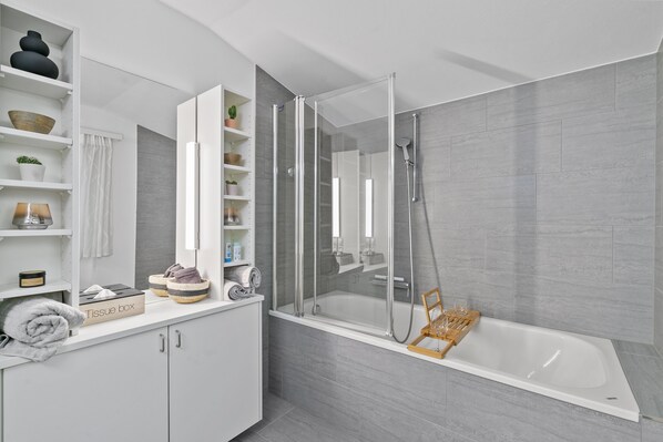 A modern bathroom with a glass-enclosed shower, a bathtub, and a vanity with shelves.