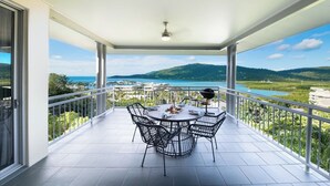 A balcony with a table and chairs, overlooking a scenic landscape with hills and a body of water. - Paradise Palms (Airlie Beach)