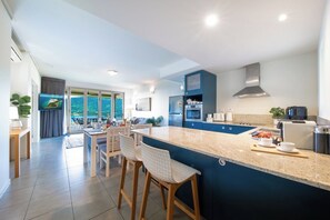 A modern kitchen with a large island, bar stools, and a view of the outdoors. - Paradise Palms (Airlie Beach)