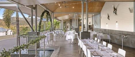 An indoor dining area with tables set for a meal, a pool, and a view of the outdoors.