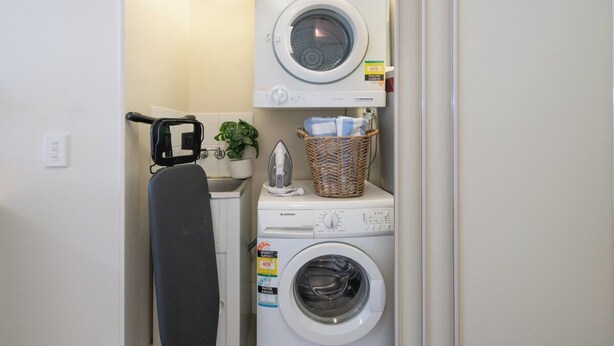 A laundry area with a washing machine, dryer, and ironing board. - Paradise Palms (Airlie Beach)