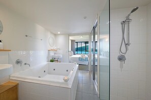 A modern bathroom with a large bathtub, a glass-enclosed shower, and a view of a pool. - Paradise Palms (Airlie Beach)