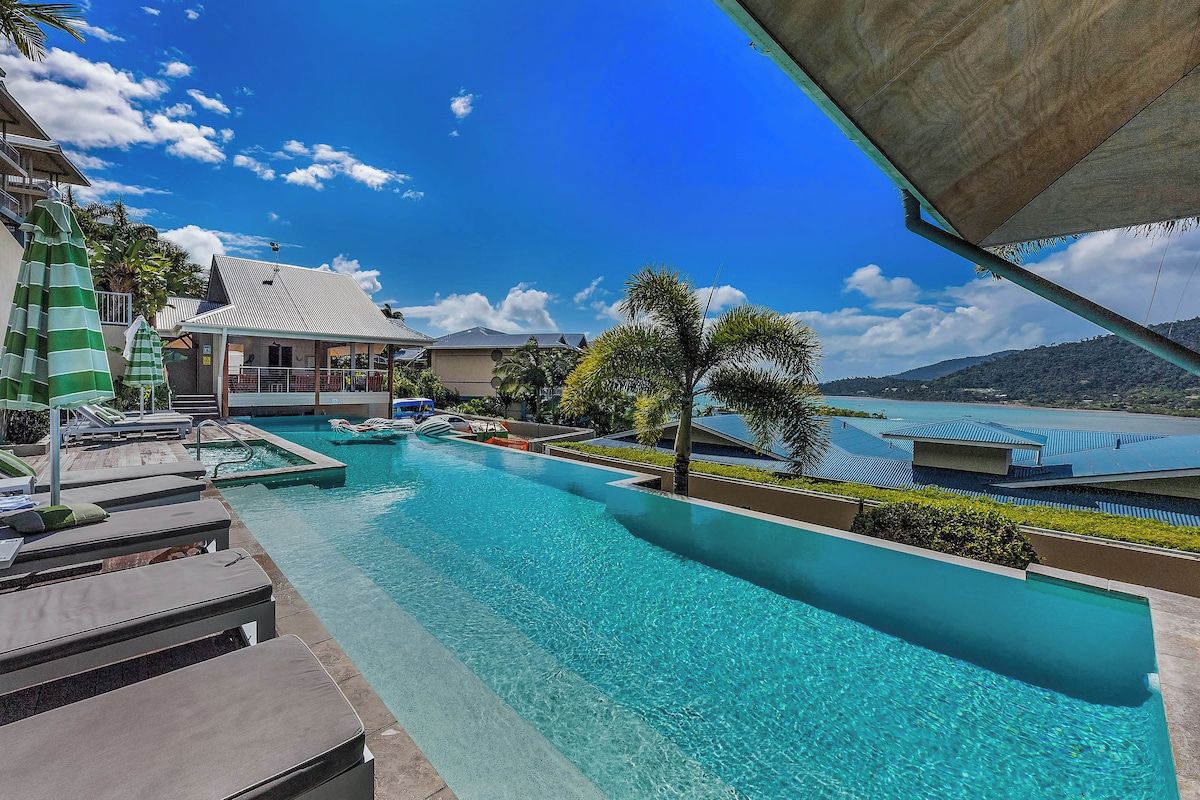 A resort pool area with lounge chairs, a water slide, and a view of the surrounding landscape.